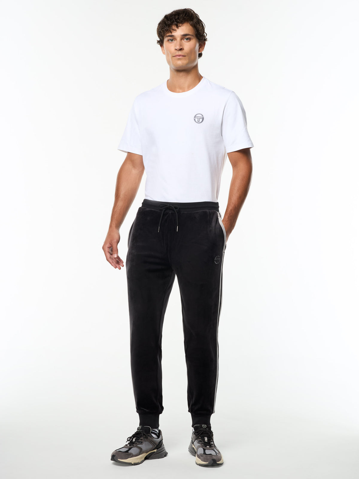 Model wearing the Damarindo Velour Track Pant in Black Beauty with a white logo tee, full body front view.