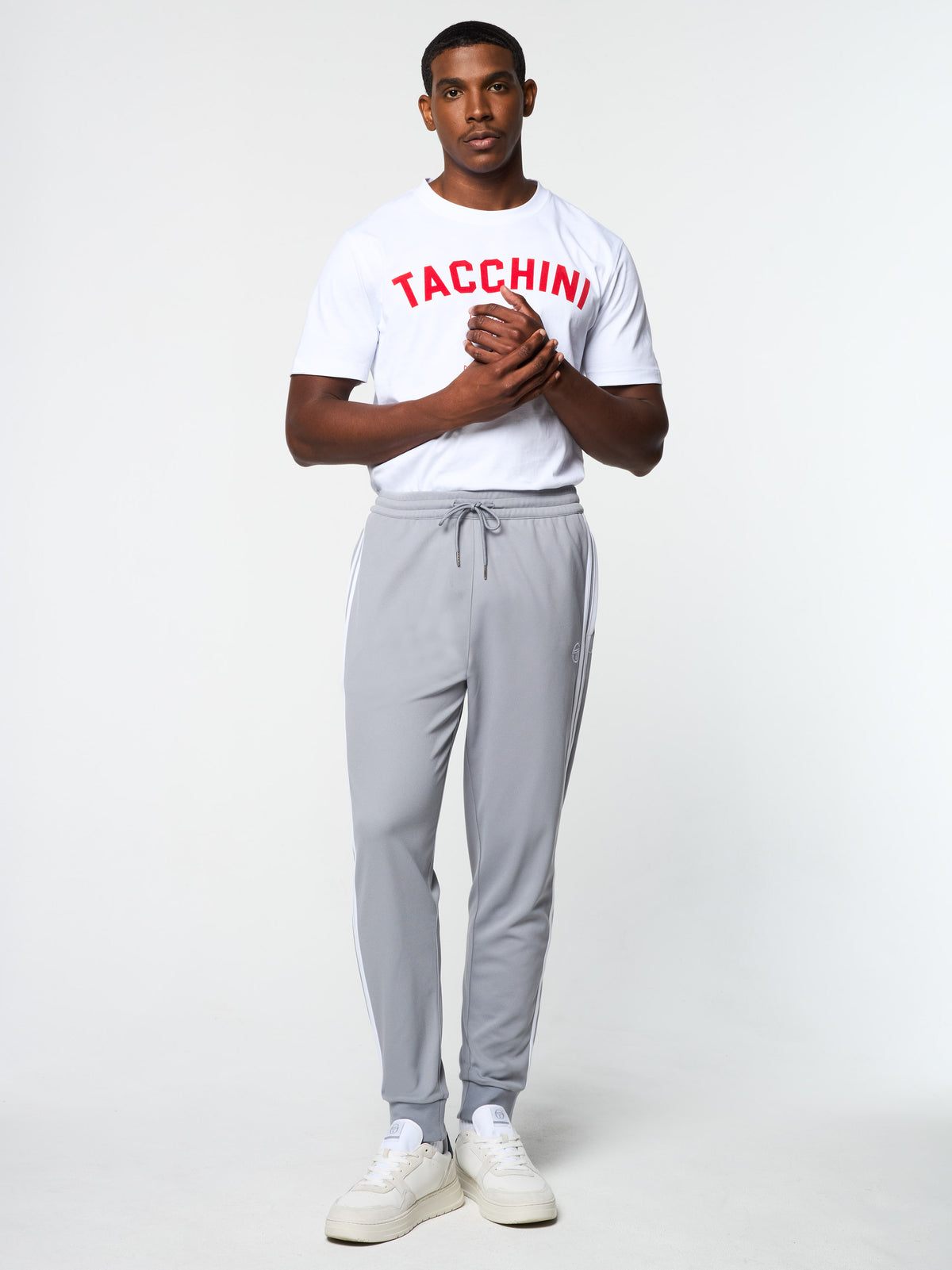 Model wearing the Damarindo Track Pant Archivio in Sleet/White with a red "TACCHINI" graphic tee, full body front view.