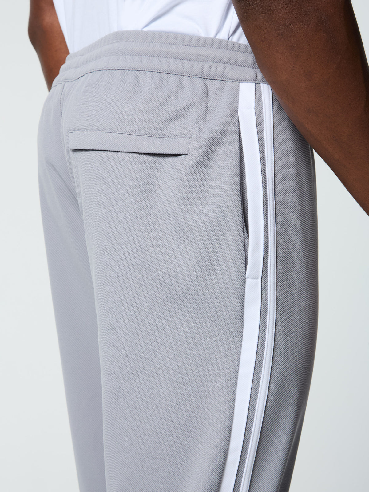 Extreme close-up of the welt back pocket and side stripe on the Damarindo Track Pant Archivio in Sleet/White.