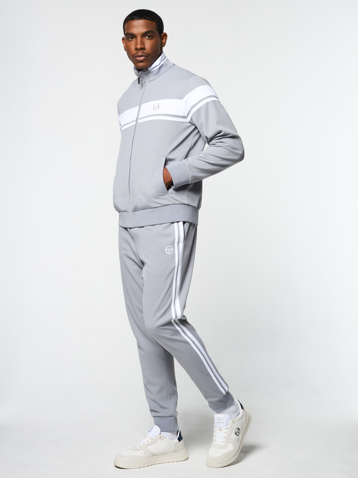 Model wearing the Damarindo Track Jacket Archivio and side-stripe pants in Sleet/White, angled side view.