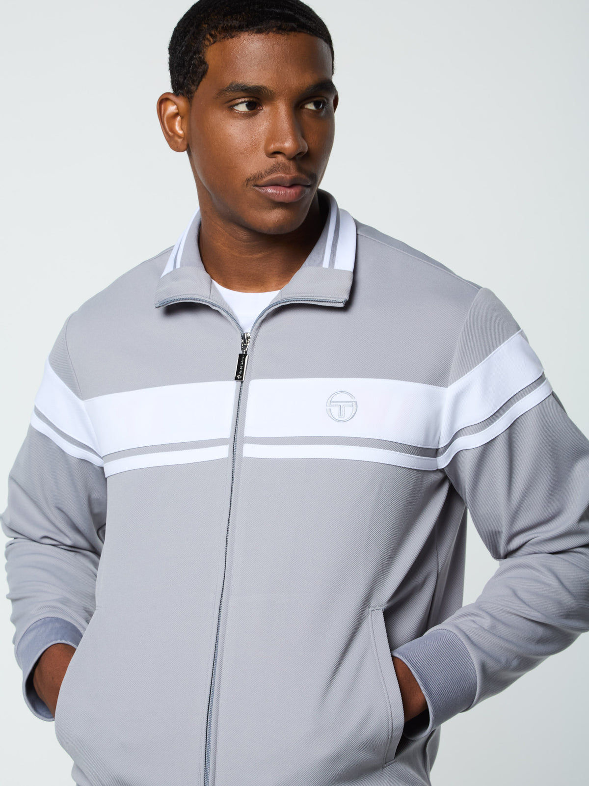 Close-up front portrait of the collar and chest logo on the Damarindo Track Jacket Archivio in Sleet/White.