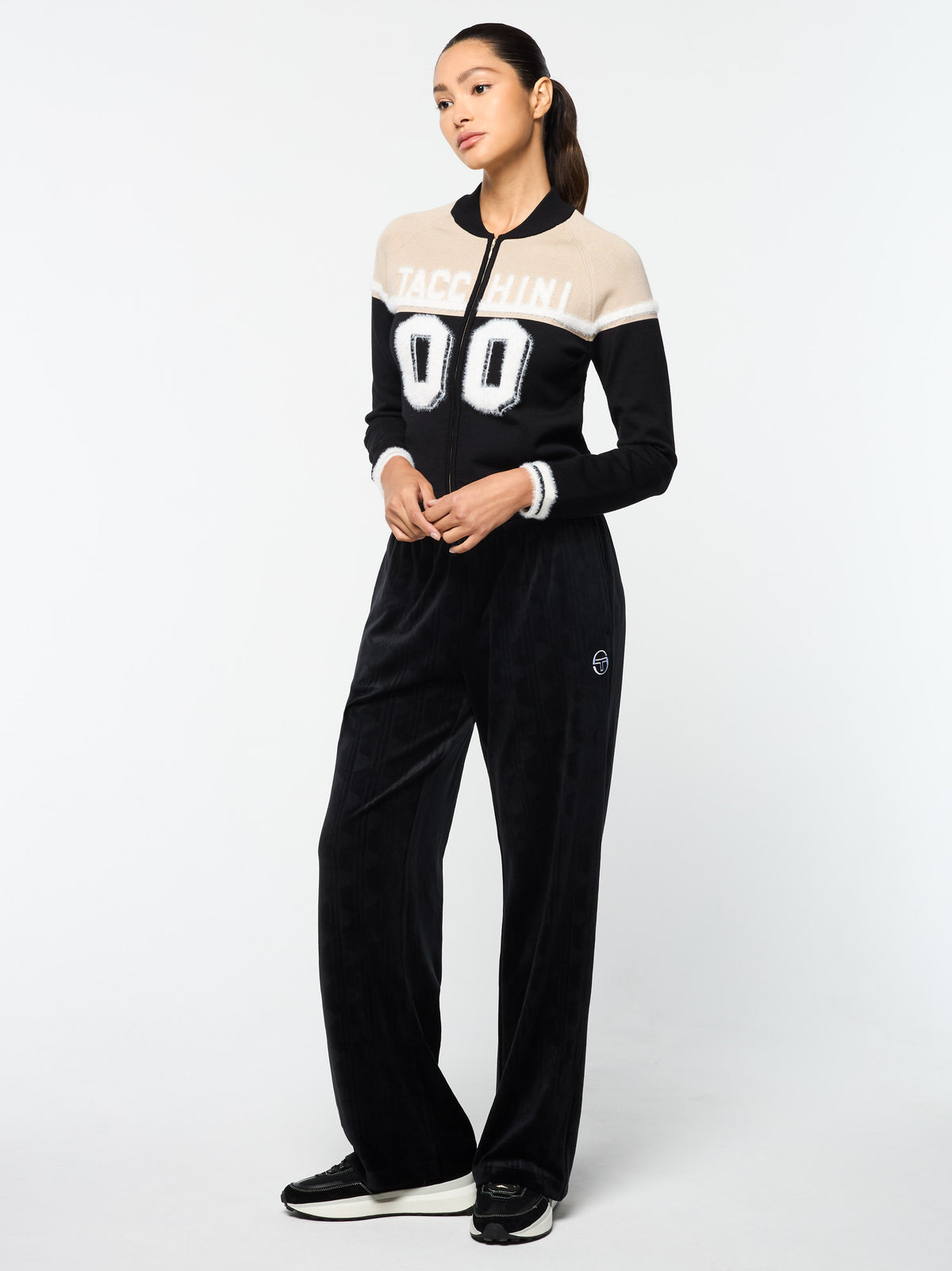 Model wearing the Ruota Cycling Jersey in Black Beauty with wide-leg velour pants, full body angled view.