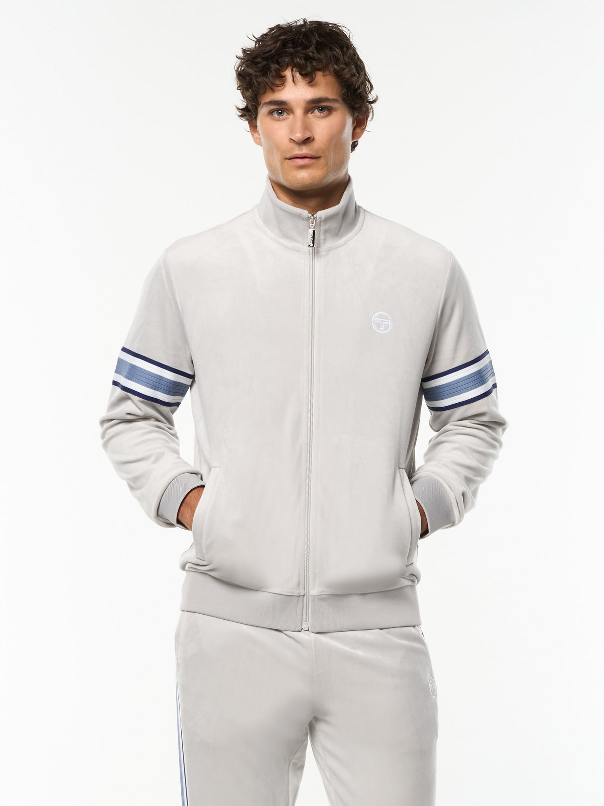 Model wearing the Linera Velour Track Jacket in Quiet Gray with blue striped sleeve bands, front upper body view.