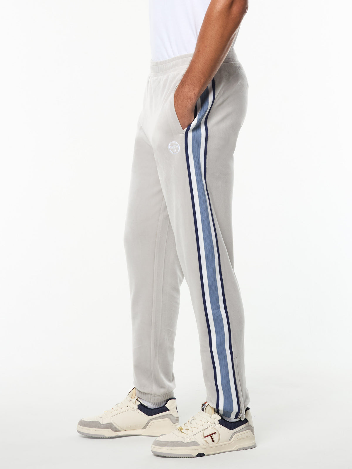 Side view of the Linera Velour Track Pant in Quiet Gray with blue side stripes, worn with cream sneakers.