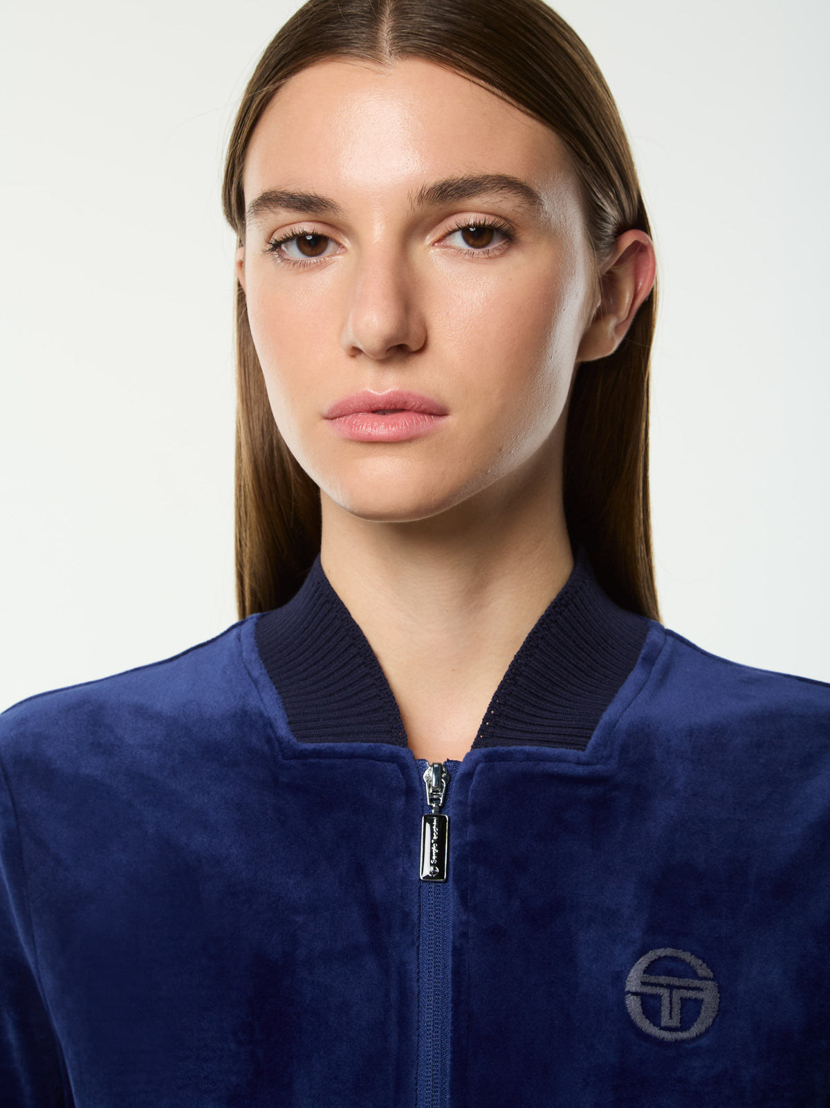 Close-up front portrait of the ribbed collar and tonal logo on the Dalia Velour Track Jacket in Beacon Blue.