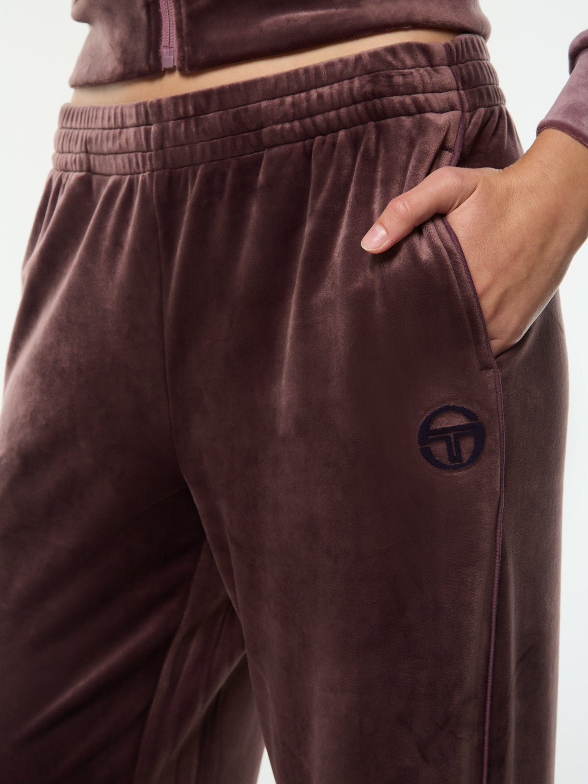 Close-up of the elastic waistband, pocket and embroidered logo on the Dalia Velour Track Pant in Huckleberry.