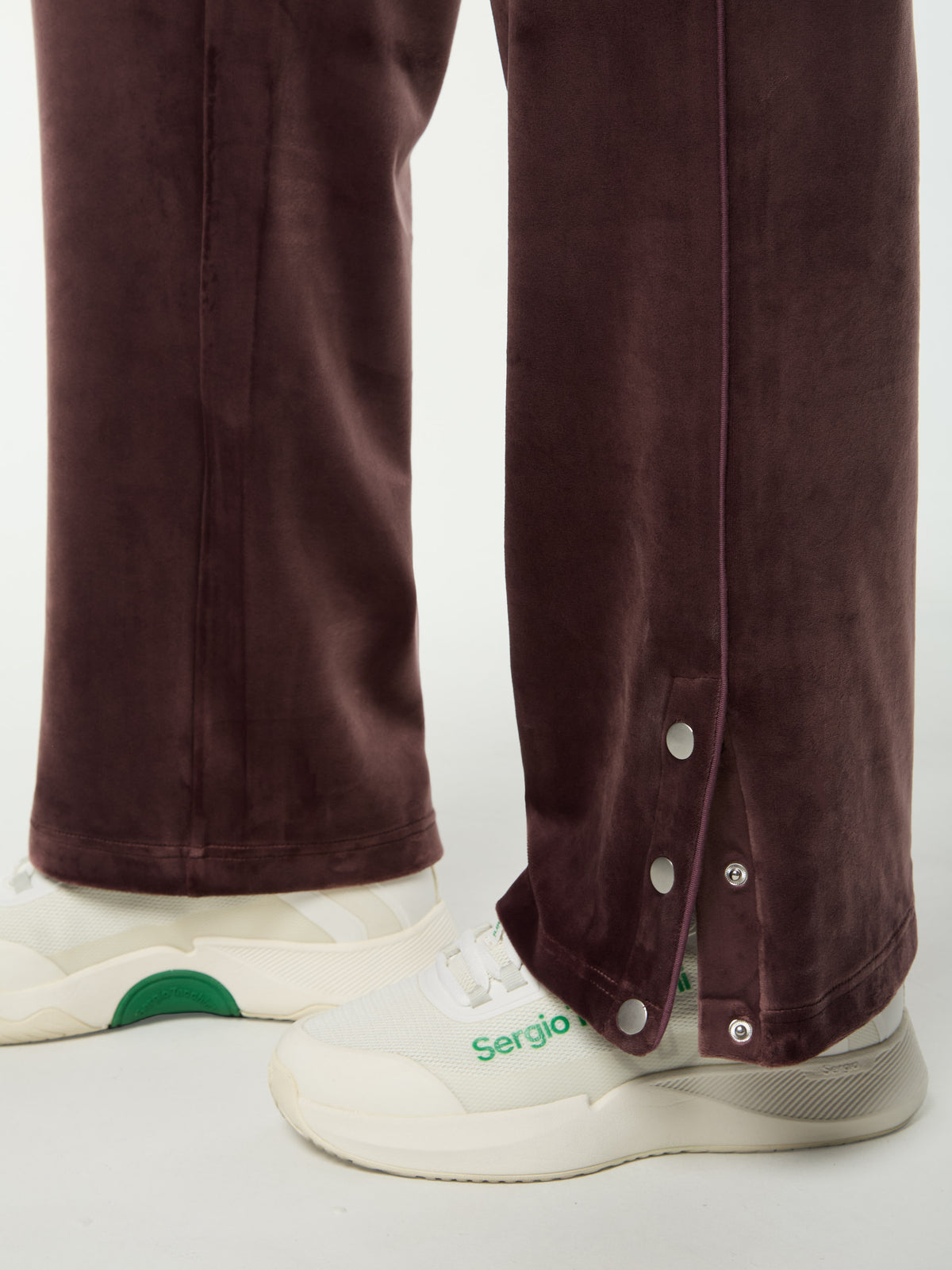Close-up of the snap-button hem on the Dalia Velour Track Pant in Huckleberry, worn with white sneakers.