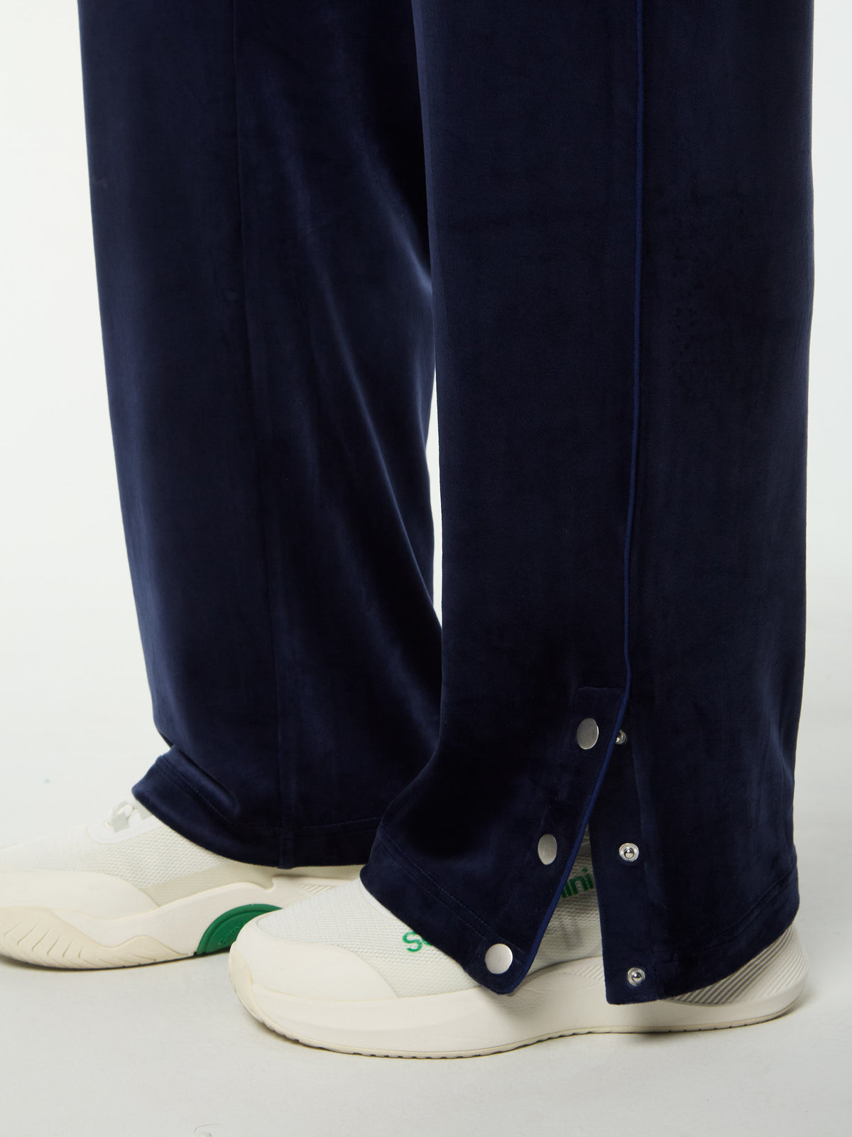 Close-up of the snap-button hem on the Dalia Velour Track Pant in Maritime Blue, worn with white sneakers.