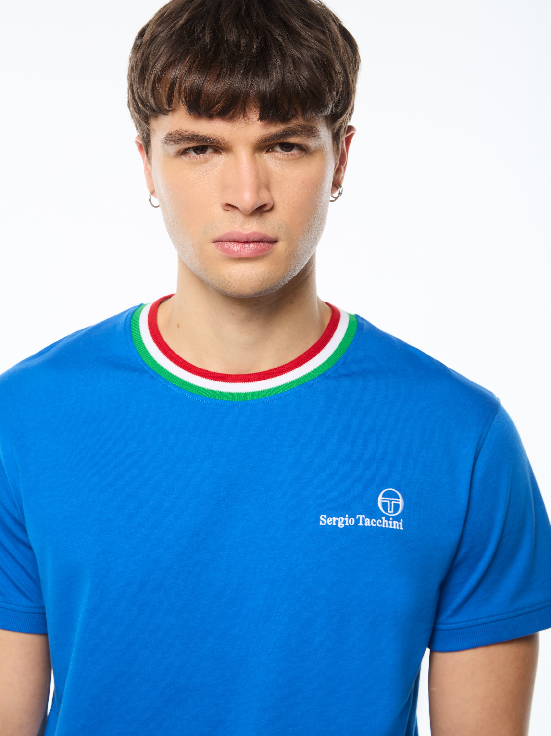 Man wearing a blue shirt with a red, white, and green stripe around collar.