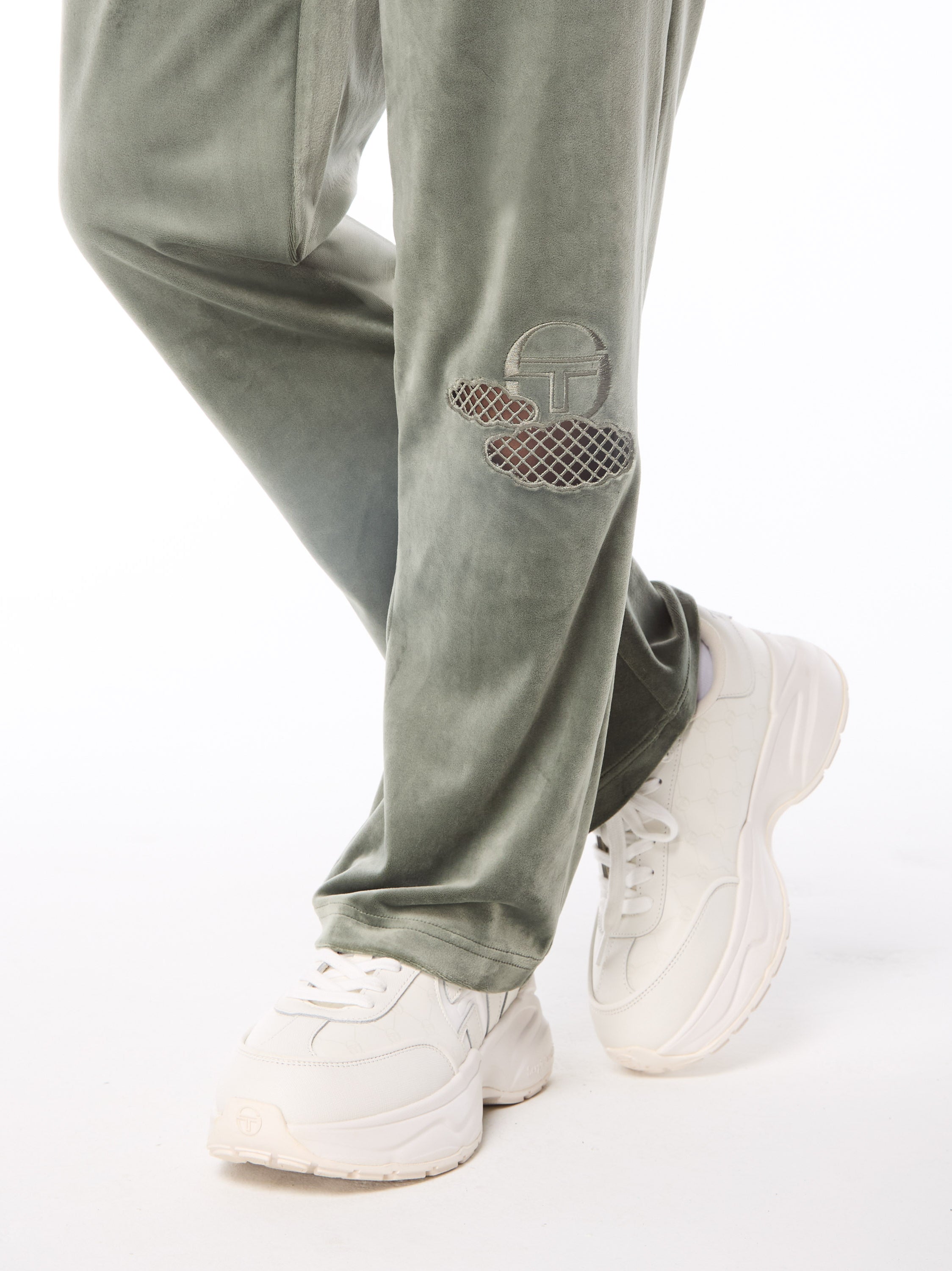 A woman wearing a sage green velvet track pant with cloud shaped cutouts on the leg.