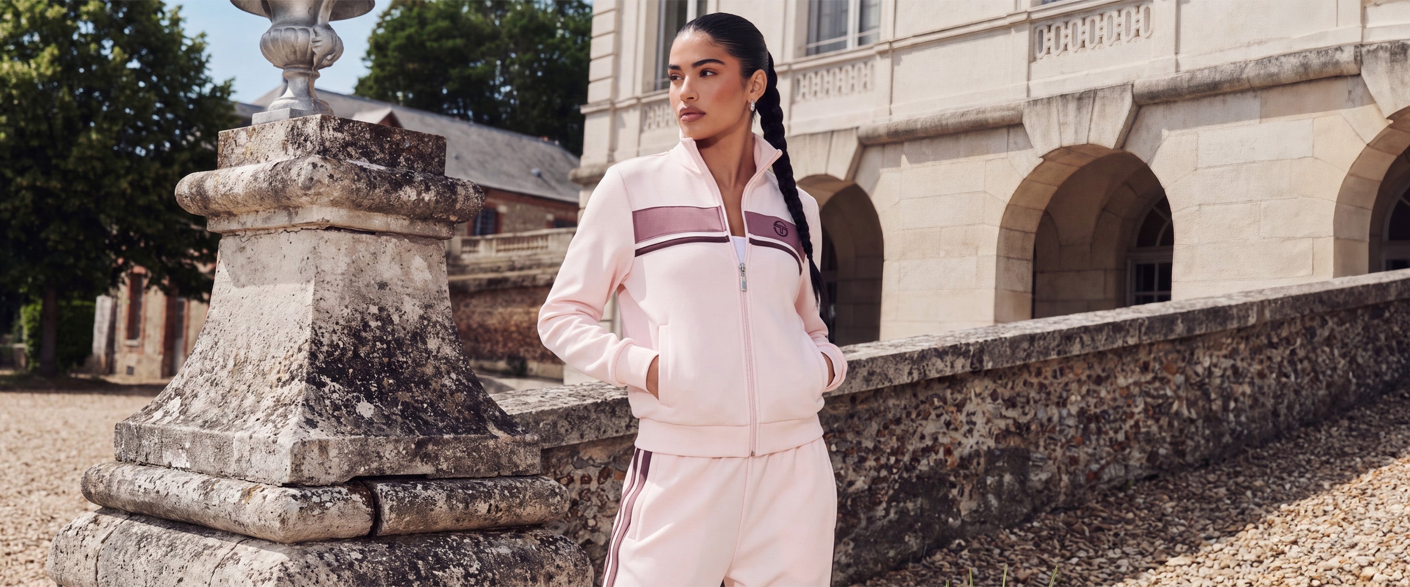 Woman standing in front of a chateau, wearing a pink tracksuit.