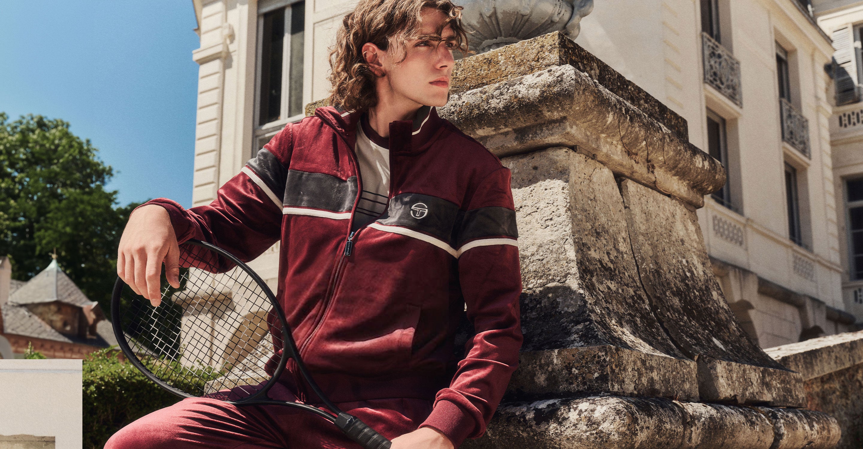 Man in maroon velour tracksuit with a tennis racket. 