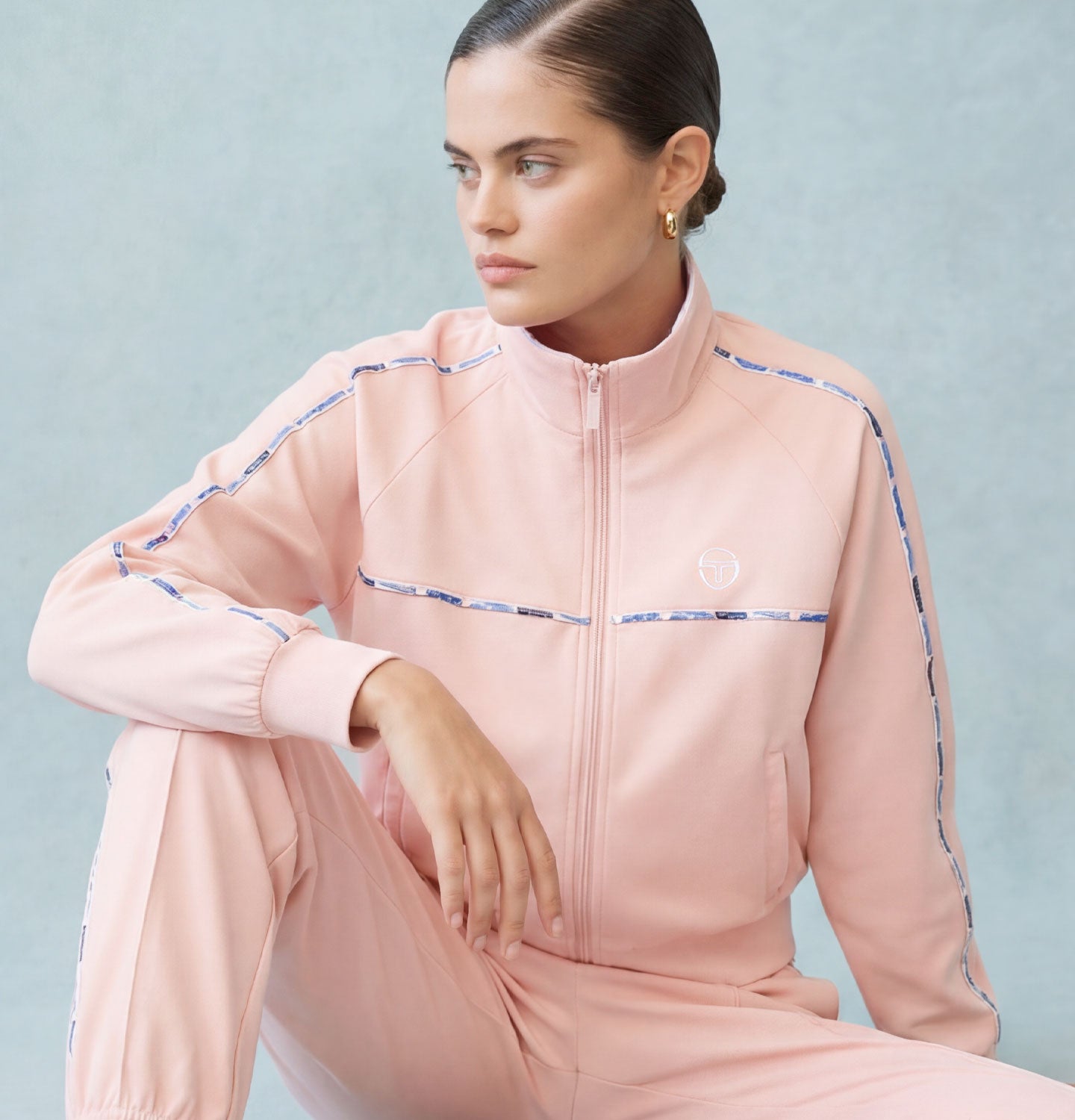 Woman wearing a baby pink tracksuit with blue accent piping.
