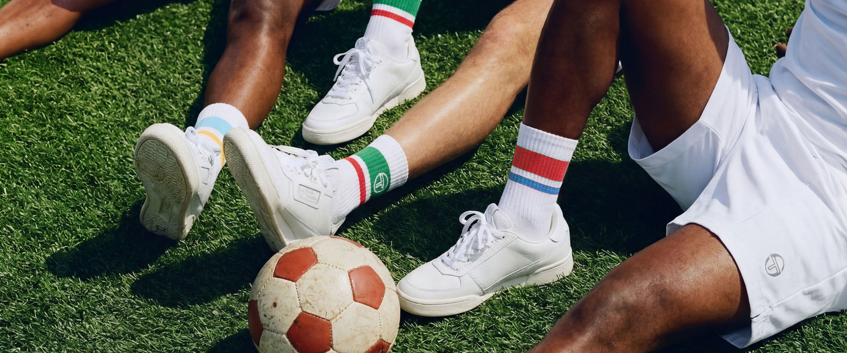 Men sitting on a soccer field wearing striped socks with a soccer ball.