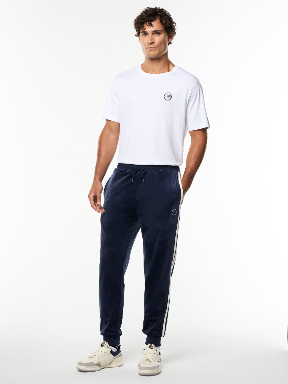 Model wearing the Damarindo Velour Track Pant in Maritime Blue with a white logo tee, full body front view.