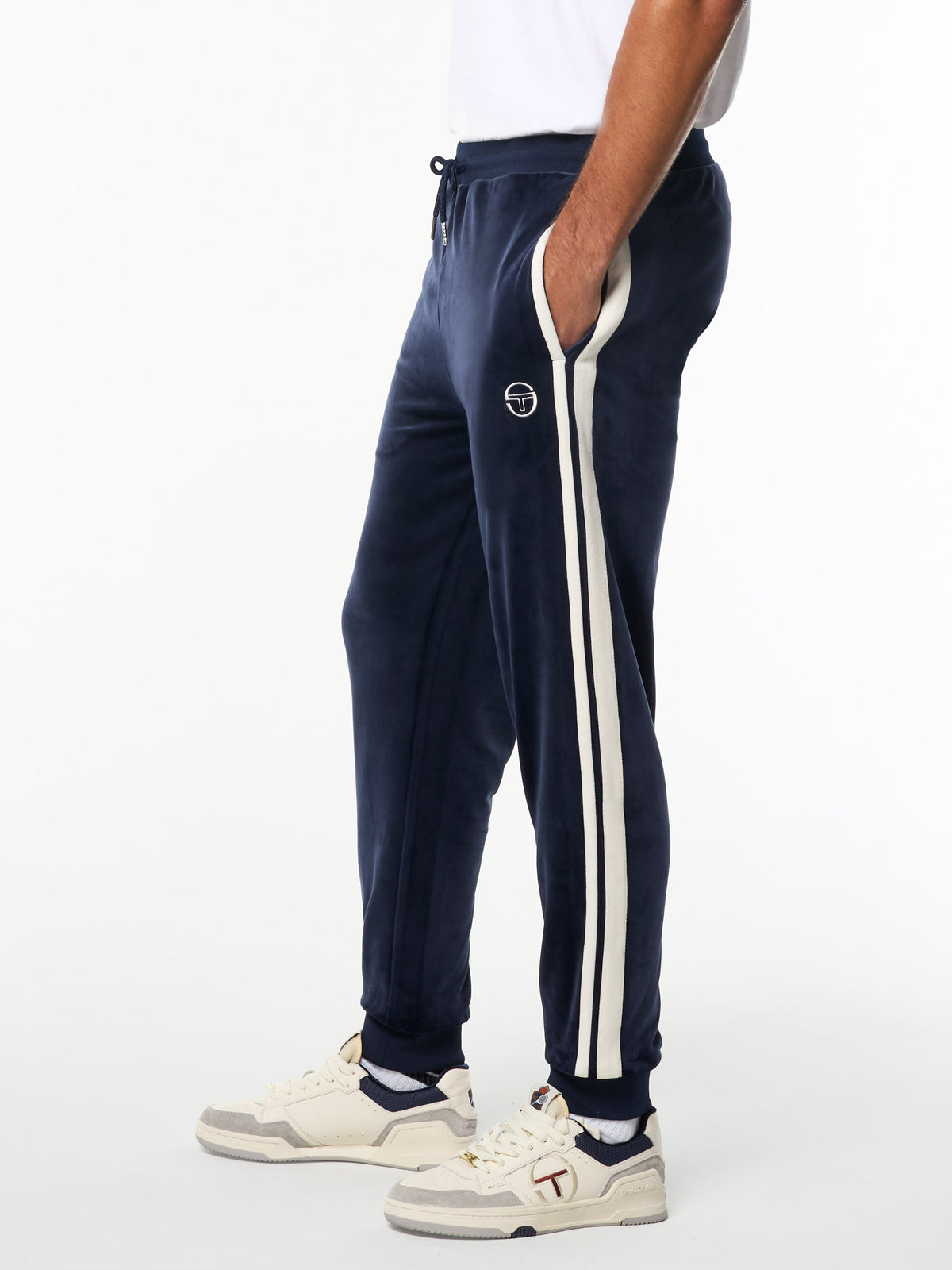 Side view of the Damarindo Velour Track Pant in Maritime Blue with white side stripes, worn with cream sneakers.