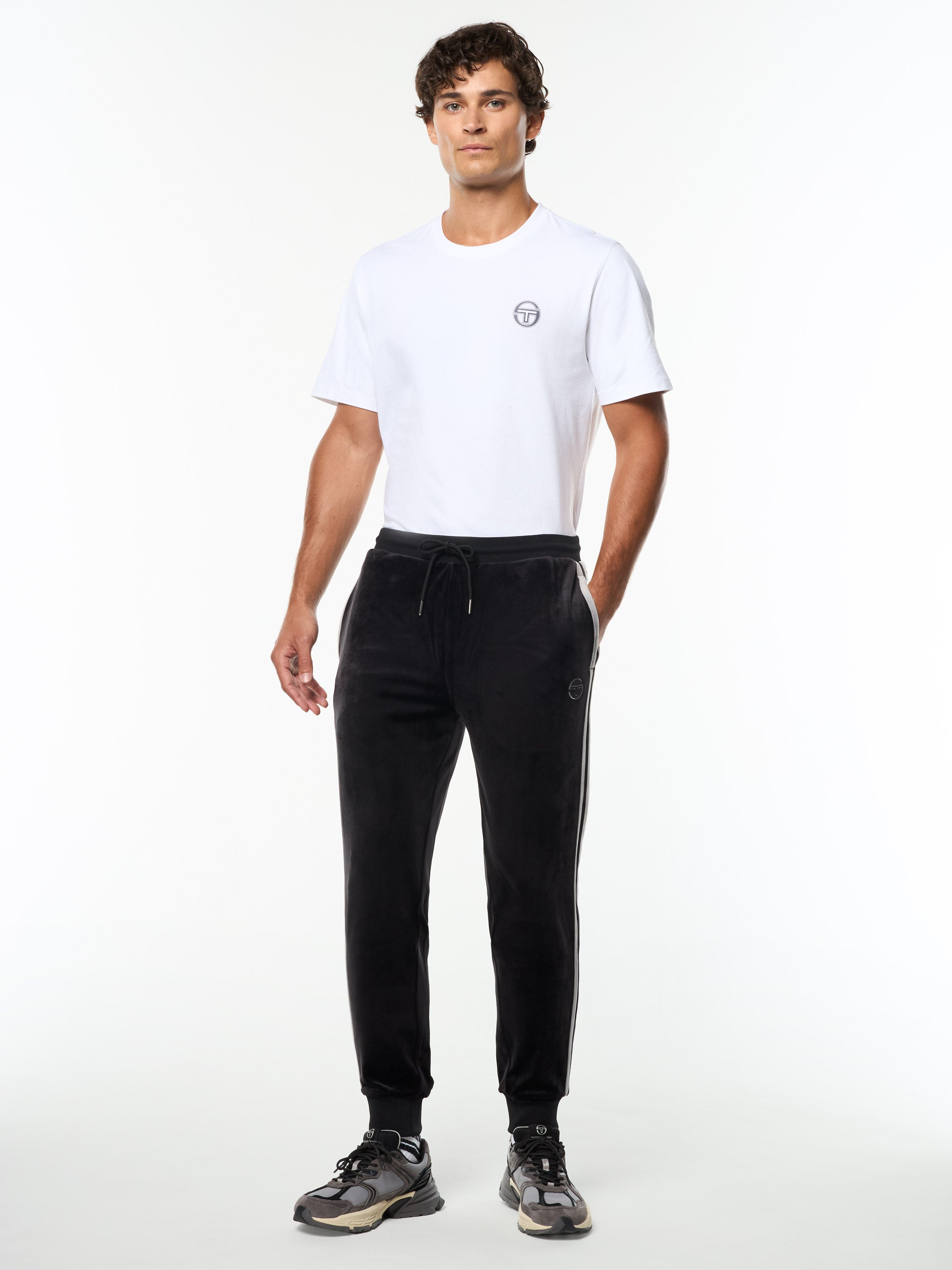 Model wearing the Damarindo Velour Track Pant in Black Beauty with a white logo tee, full body front view.