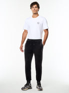 Model wearing the Damarindo Velour Track Pant in Black Beauty with a white logo tee, full body front view.