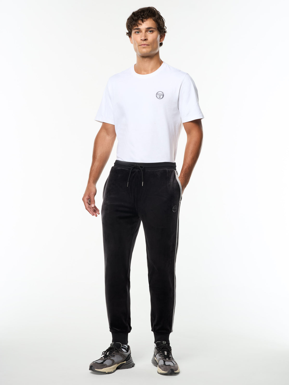 Model wearing the Damarindo Velour Track Pant in Black Beauty with a white logo tee, full body front view.