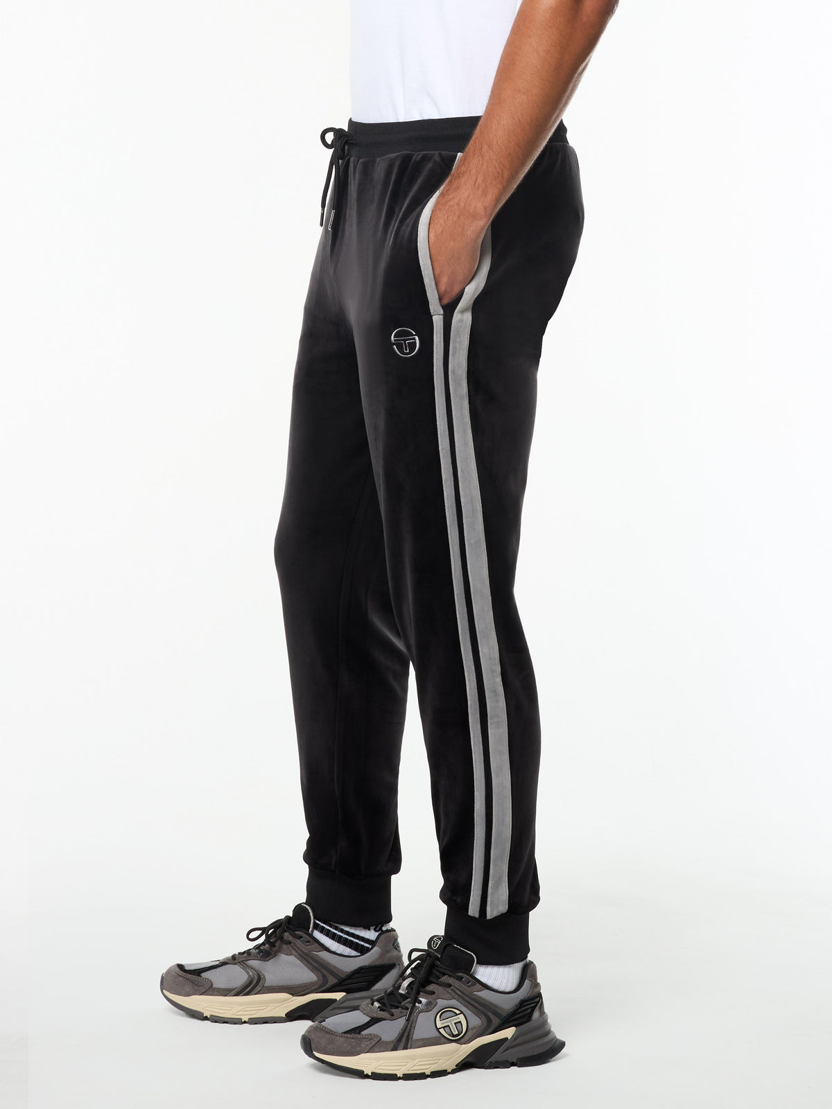 Side view of the Damarindo Velour Track Pant in Black Beauty with gray side stripes, worn with gray sneakers.