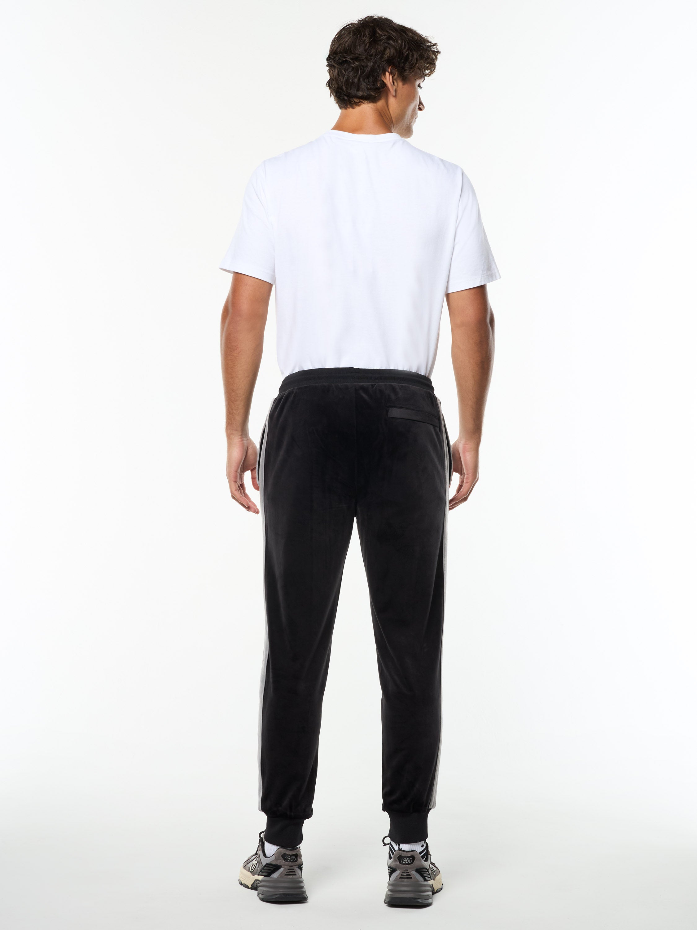 Full body back view of the Damarindo Velour Track Pant in Black Beauty worn with a white tee.