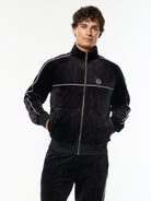 Model wearing the Lioni Velour Track Jacket in Black Beauty with white piping, front upper body view.