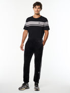 Model wearing the Lioni Velour Track Pant in Black Beauty with a black and gray striped tee, full body front view.