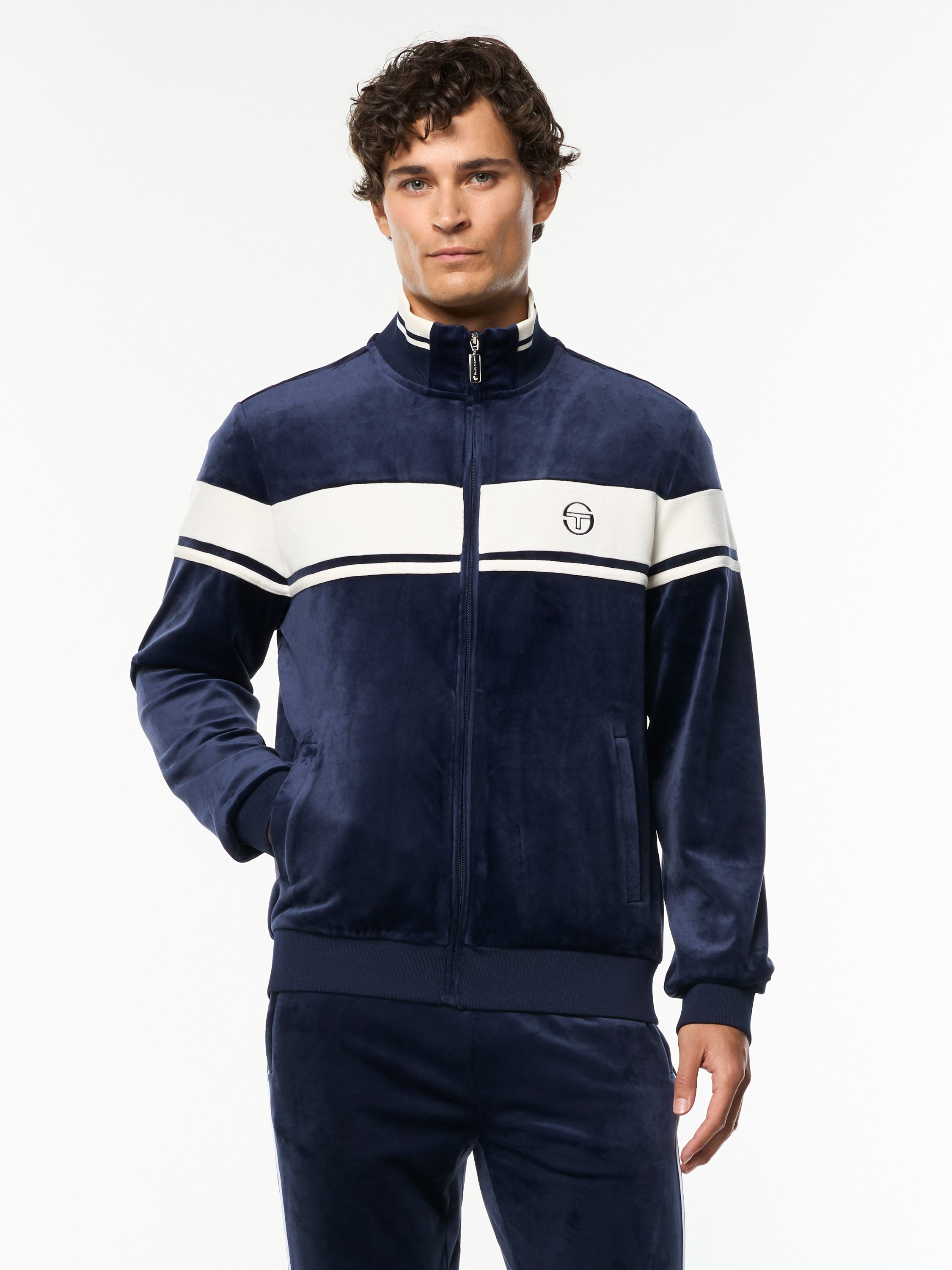 Model wearing the Damarindo Velour Track Jacket in Maritime Blue with a white chest stripe, front upper body view.