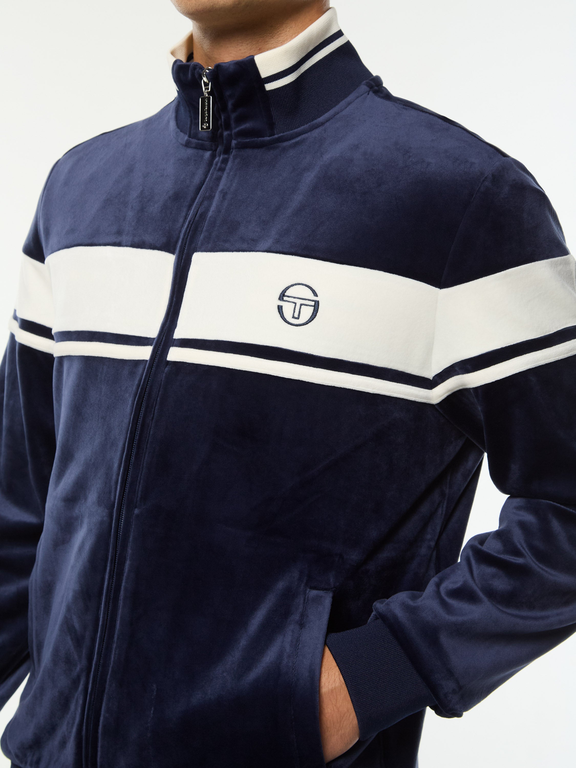 Close-up of the chest stripe, logo and zip pocket on the Damarindo Velour Track Jacket in Maritime Blue.