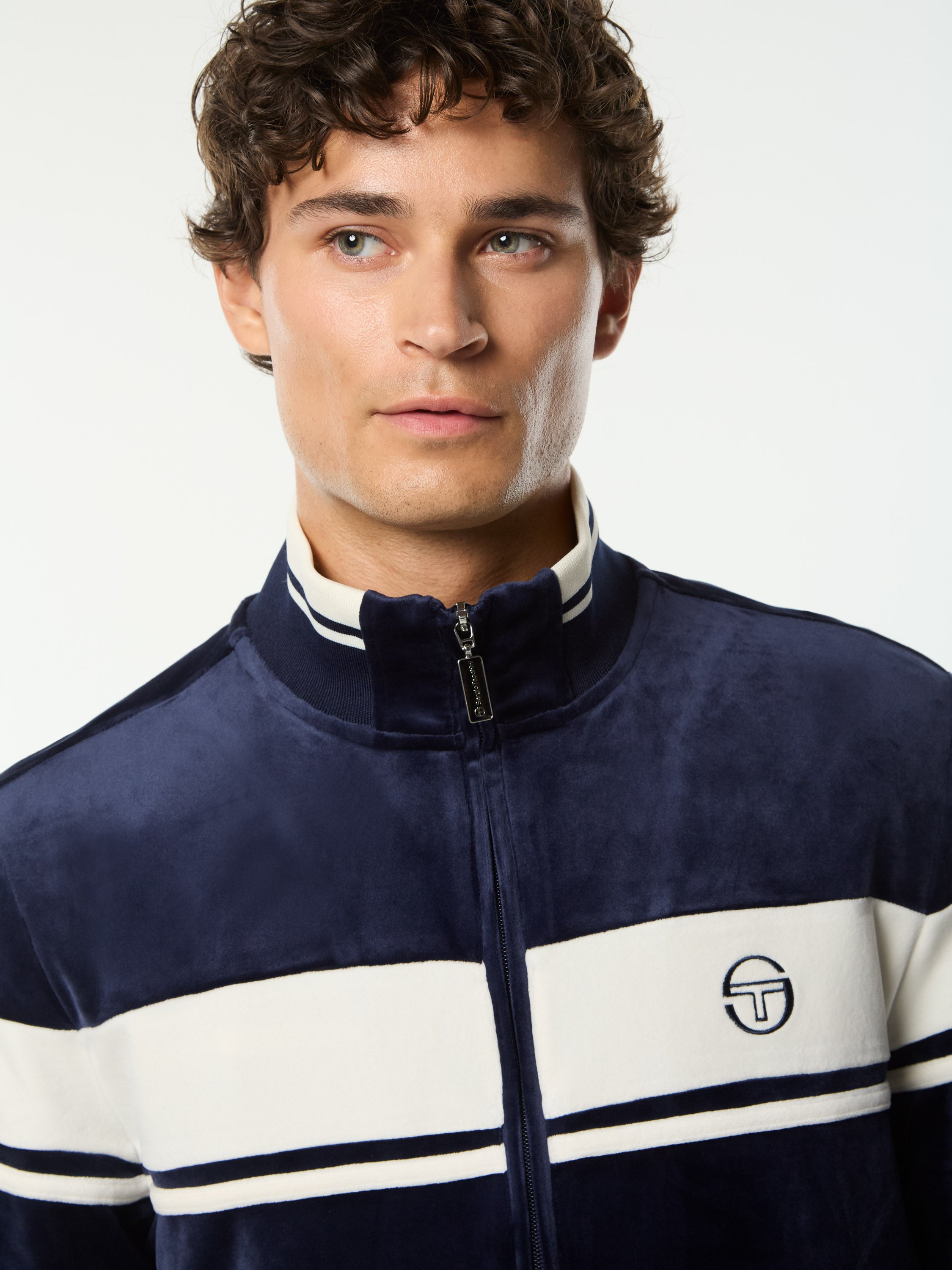 Close-up front portrait of the stand collar and embroidered logo on the Damarindo Velour Track Jacket in Maritime Blue.