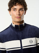 Close-up front portrait of the stand collar and embroidered logo on the Damarindo Velour Track Jacket in Maritime Blue.