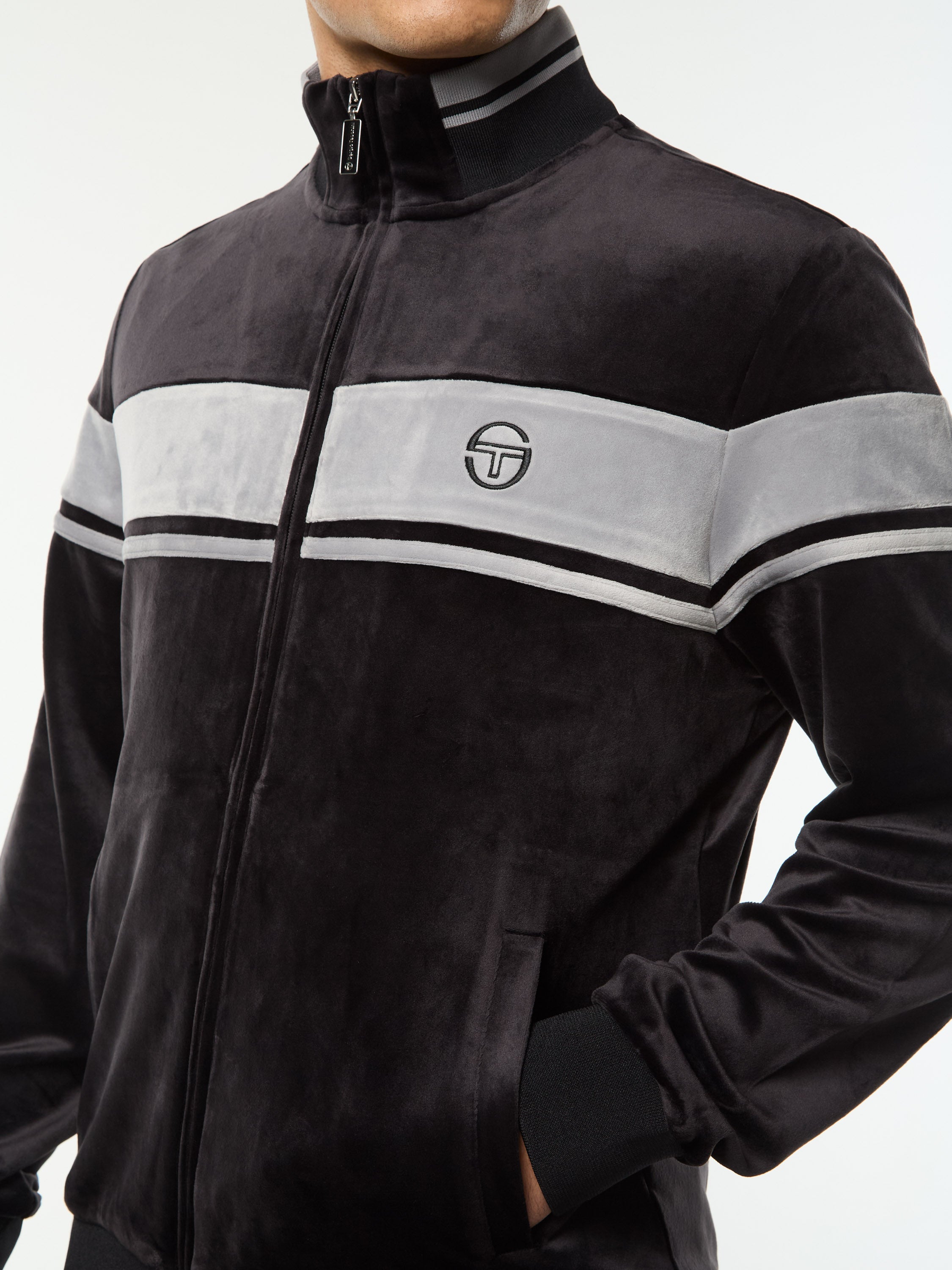Close-up of the chest stripe, logo and zip on the Damarindo Velour Track Jacket in Black Beauty.