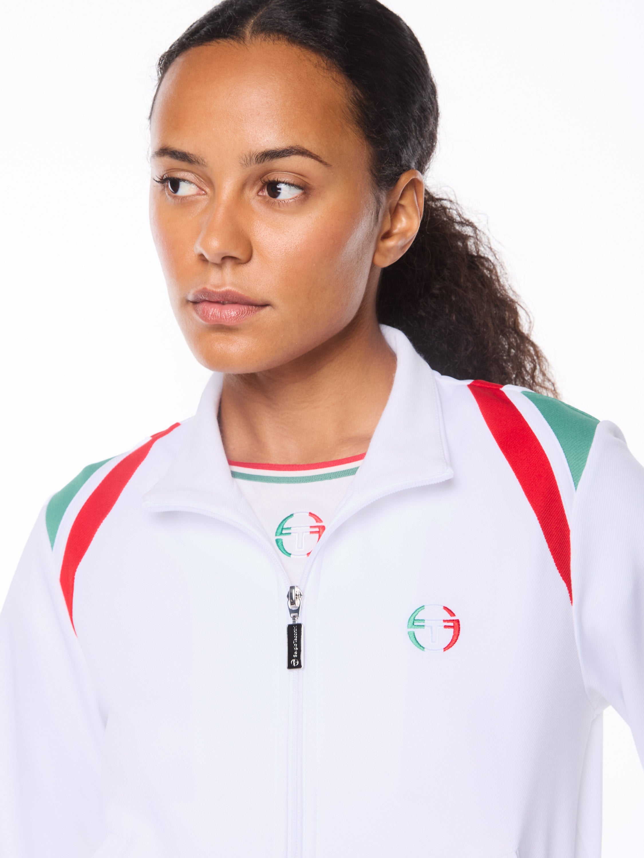 Woman wearing a white track jacket with red and green accent details.