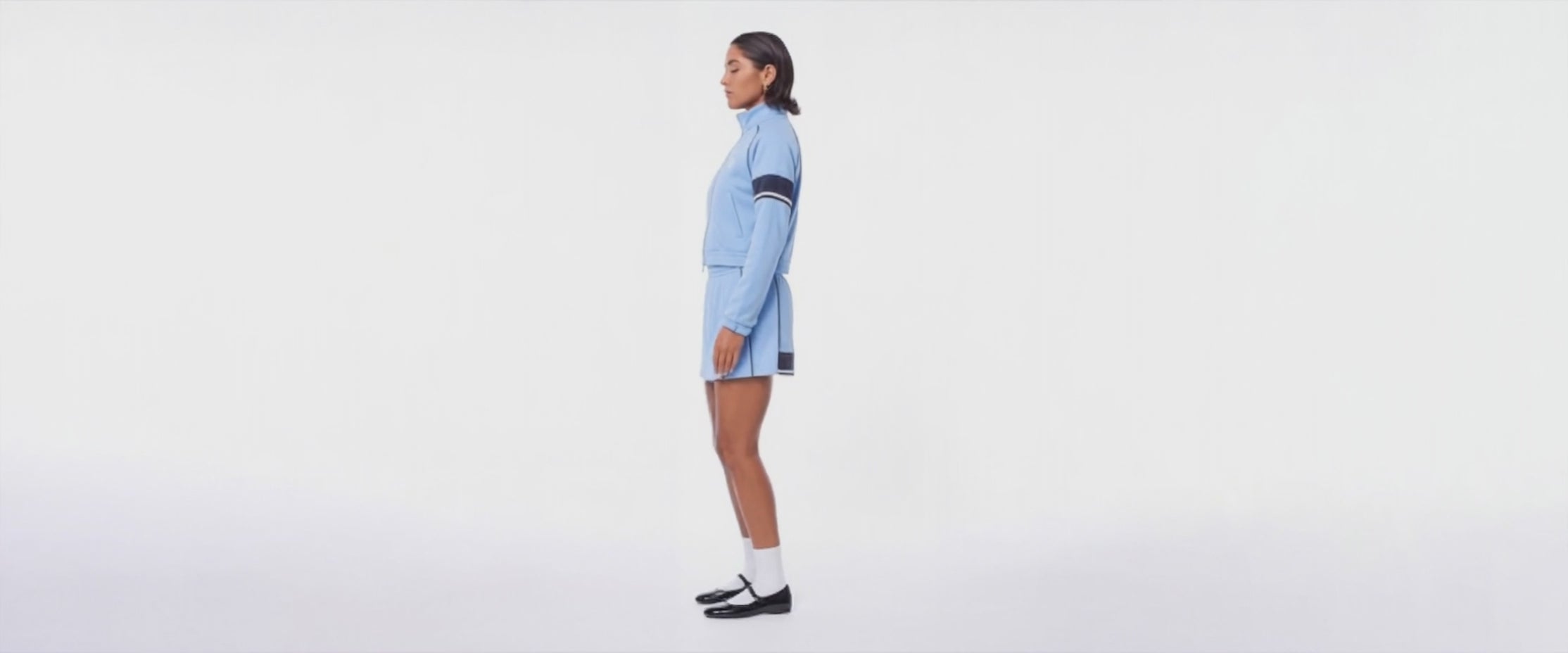 Woman turning around in a circle showing off the baby blue track jacket and matching skirt that she's wearing.